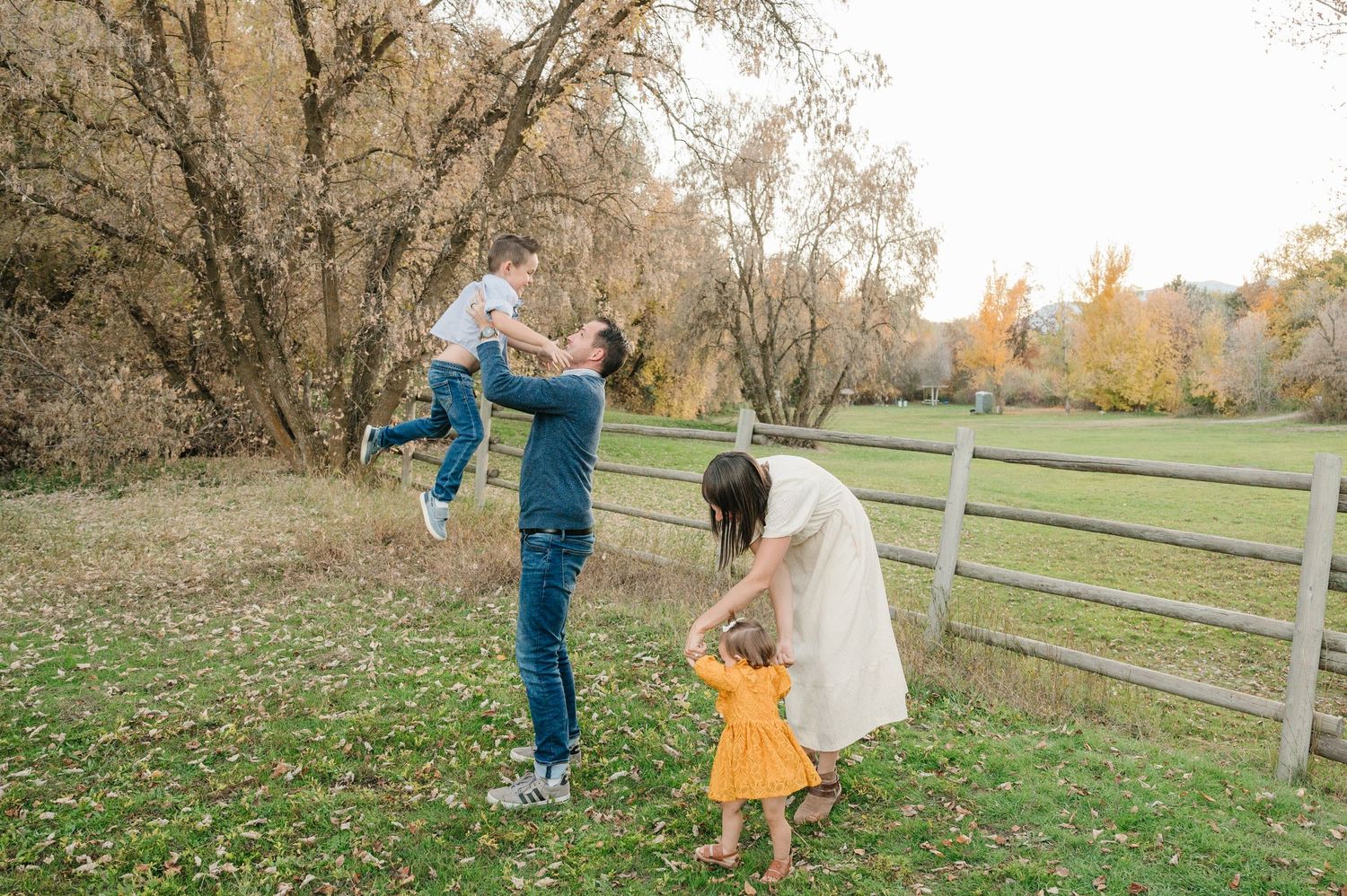 Playful family moment in front of rustic fence during autumn.