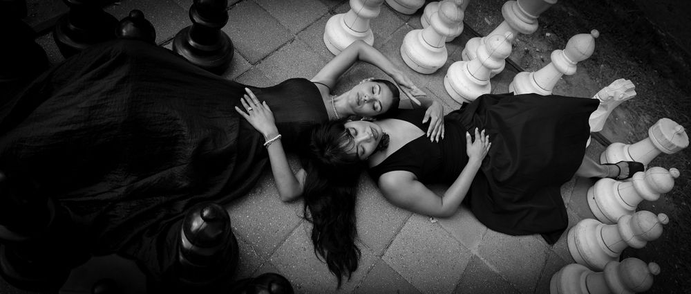 Black and white photo of someone laying on ground near chess pieces.