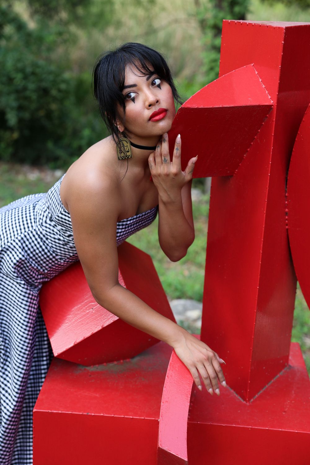 Fashion portrait with model posing against a bright red geometric sculpture outdoors.