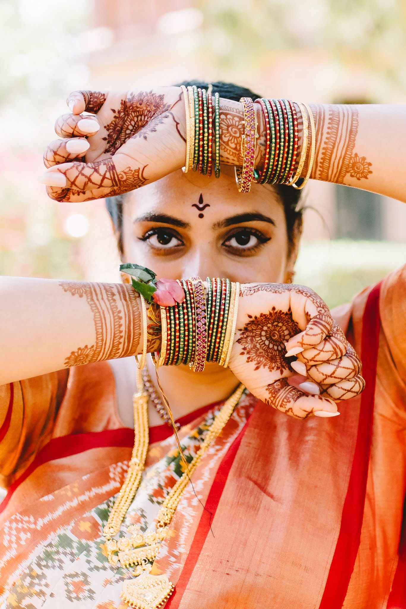 Indian bride showcasing intricate henna mehndi designs on hands, wearing colorful bangles and traditional red saree.