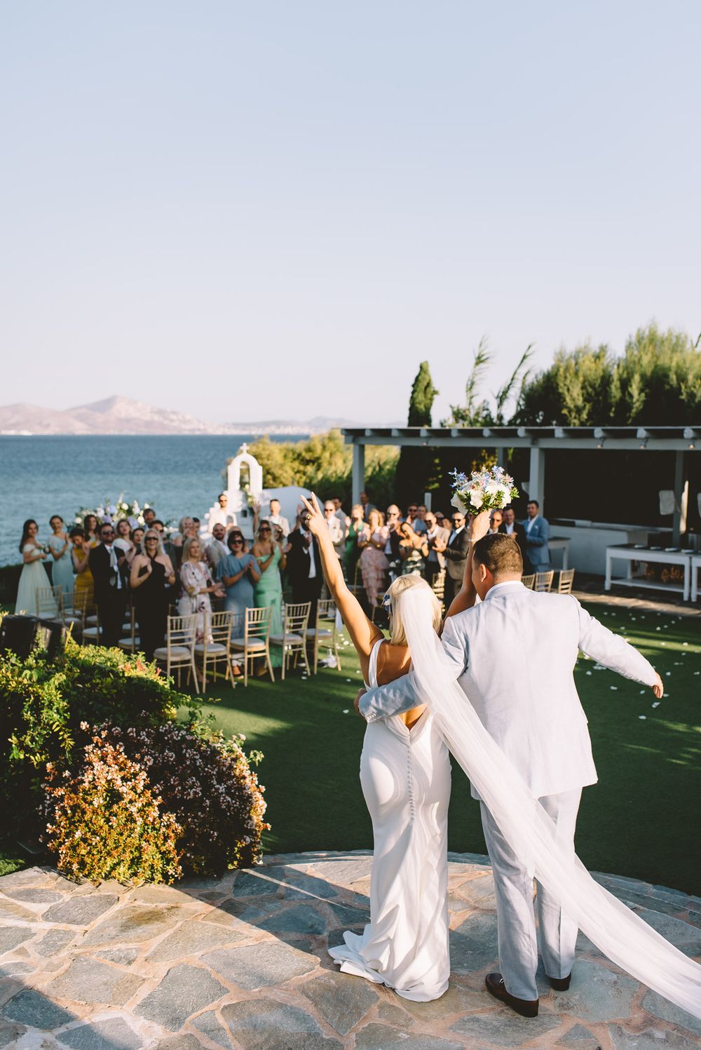Wedding celebration on a scenic seaside terrace with guests cheering the newlyweds.
