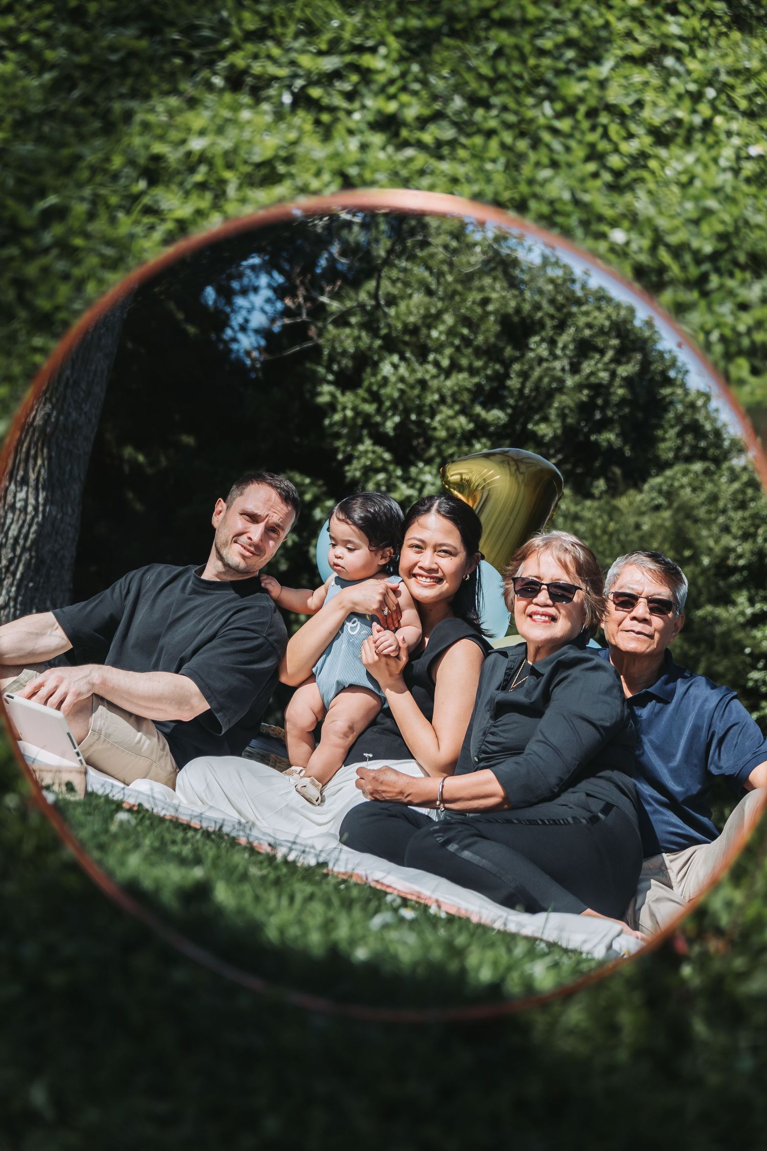Family gathering captured through a round mirror frame surrounded by lush greenery.