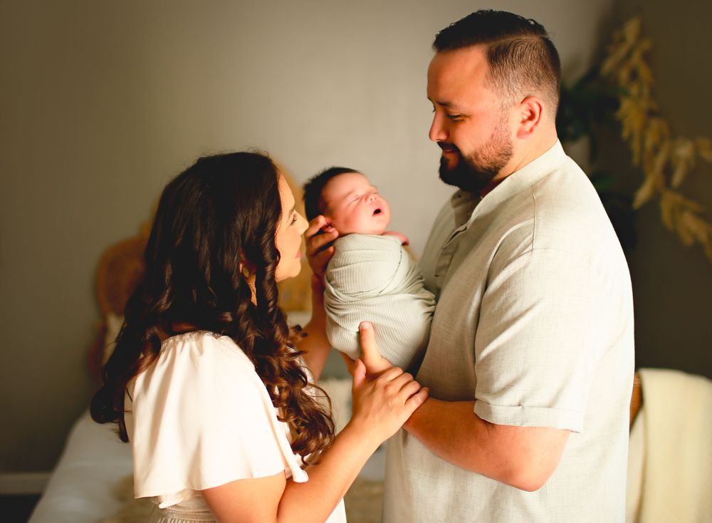 New mom and dad stare at one another while holding newborn baby at Alvin, Tx studio