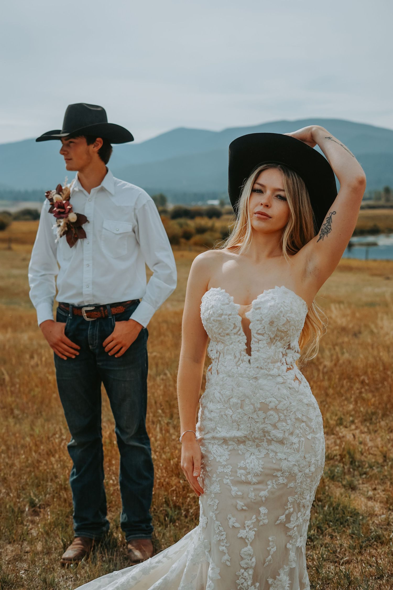 A western-themed wedding photo showing a couple in a field with mountains in the background.