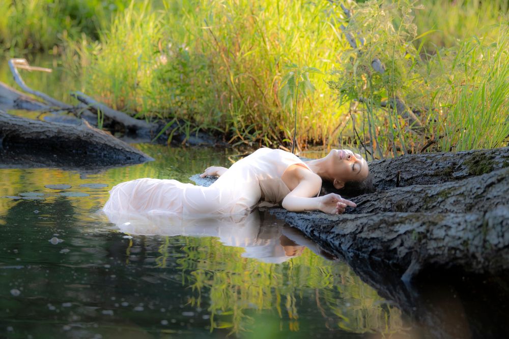 Peaceful scene of figure reclining on dark rocks beside still water.