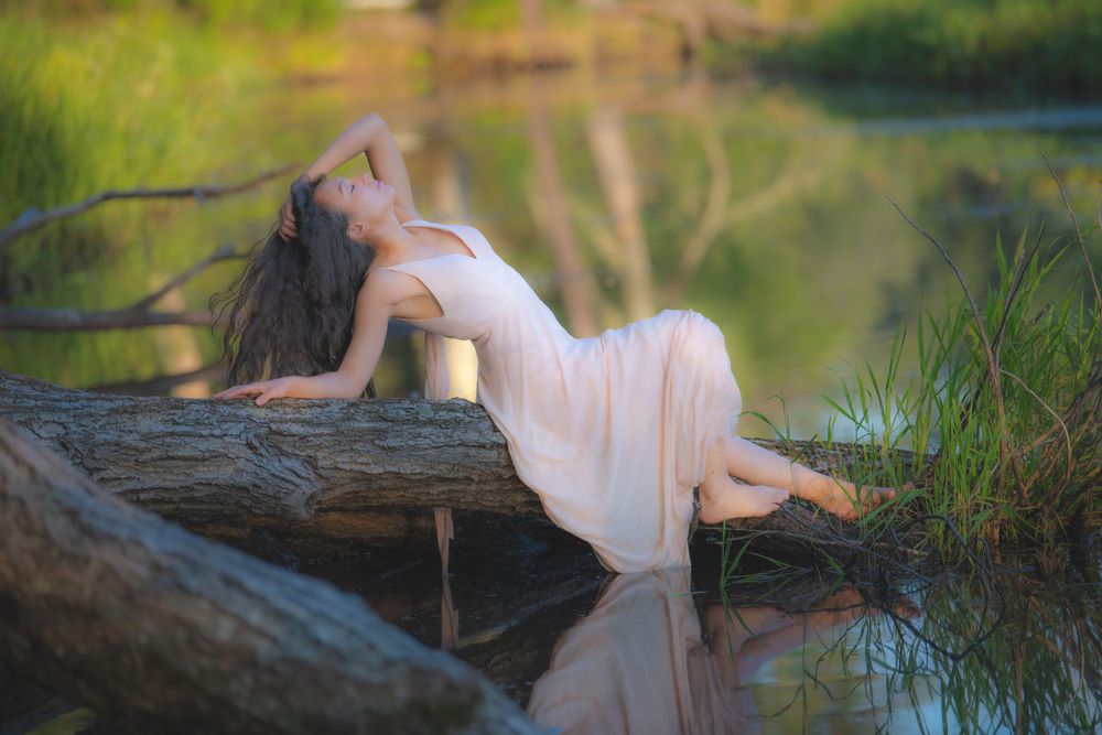 Artistic nature portrait with graceful pose on fallen log over tranquil water.