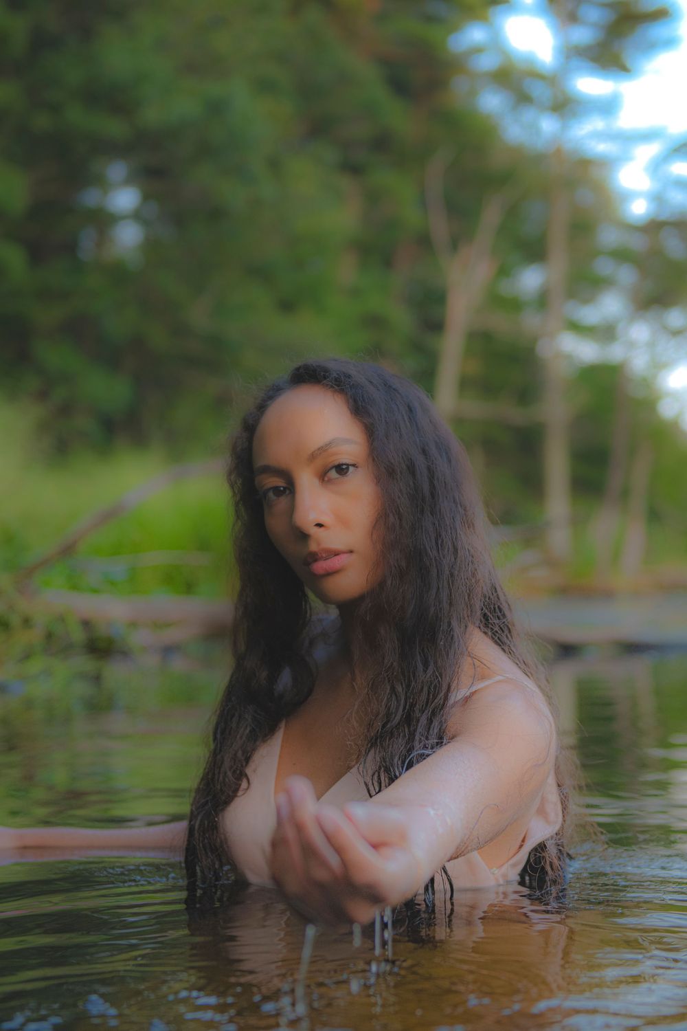 Ethereal portrait in a forest lake with soft lighting and reflective water creating a dreamy atmosphere.