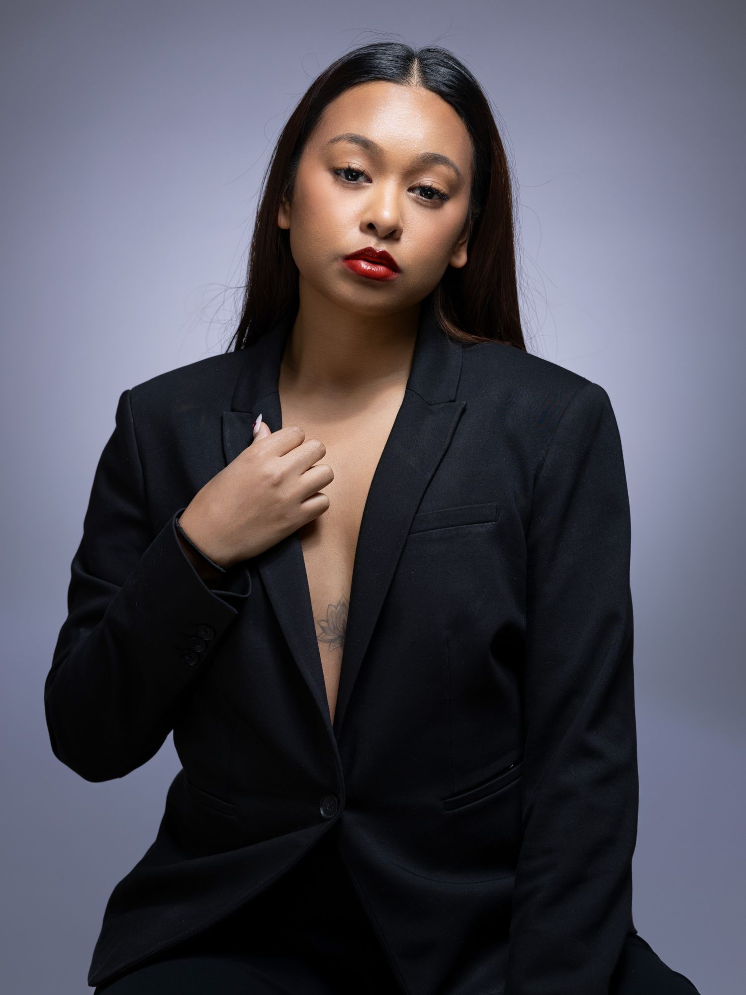 Professional studio portrait of a model in black blazer with bold red lipstick against grey background.