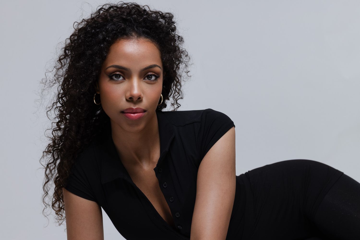 Portrait of someone wearing a black top with curly dark hair against a light background.