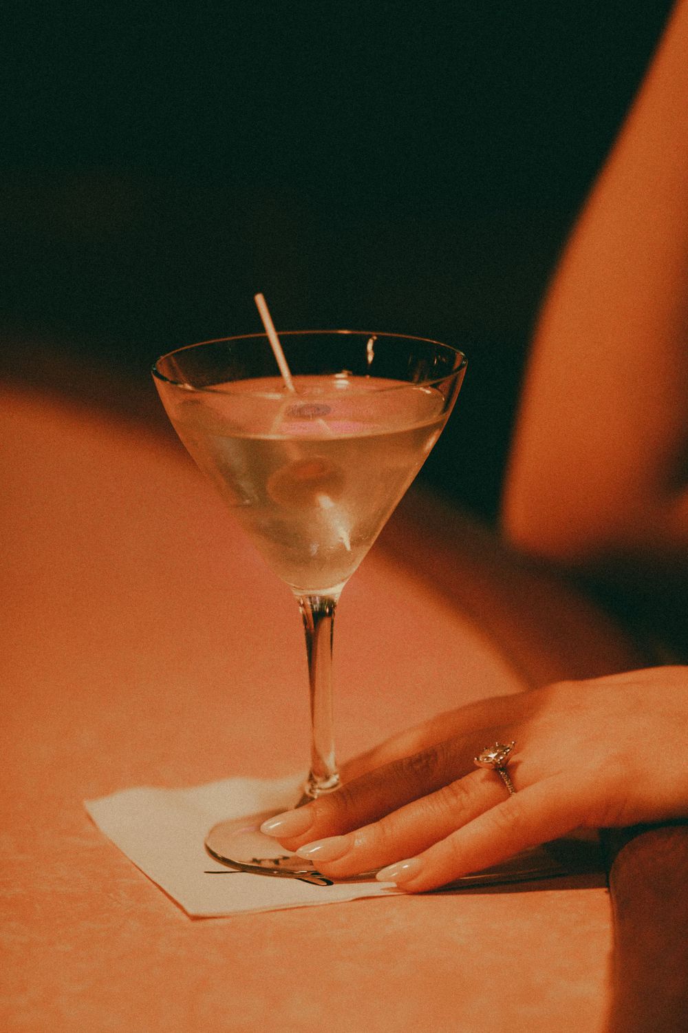 Martini glass with cocktail and hand resting on napkin in moody lighting.