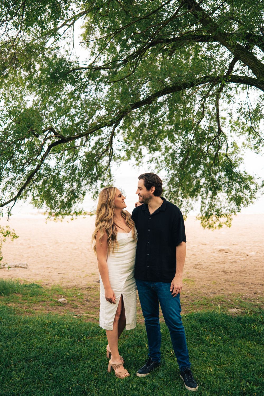 Couple standing together under green tree branches.