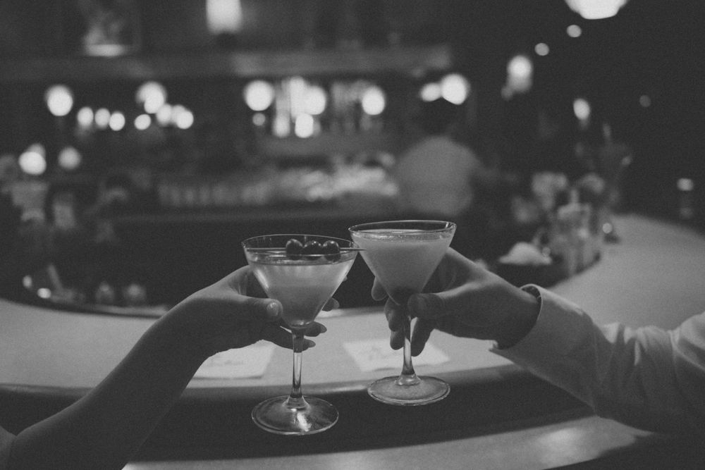Two martini glasses clinking together in black and white nighttime setting.