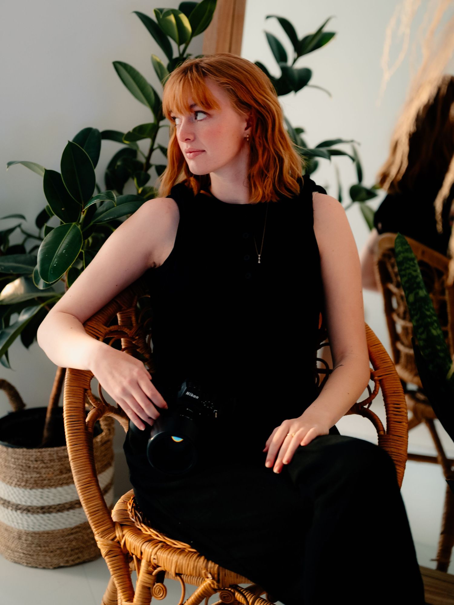 Indoor lifestyle photoshoot with a rattan chair and monstera plants in the background.