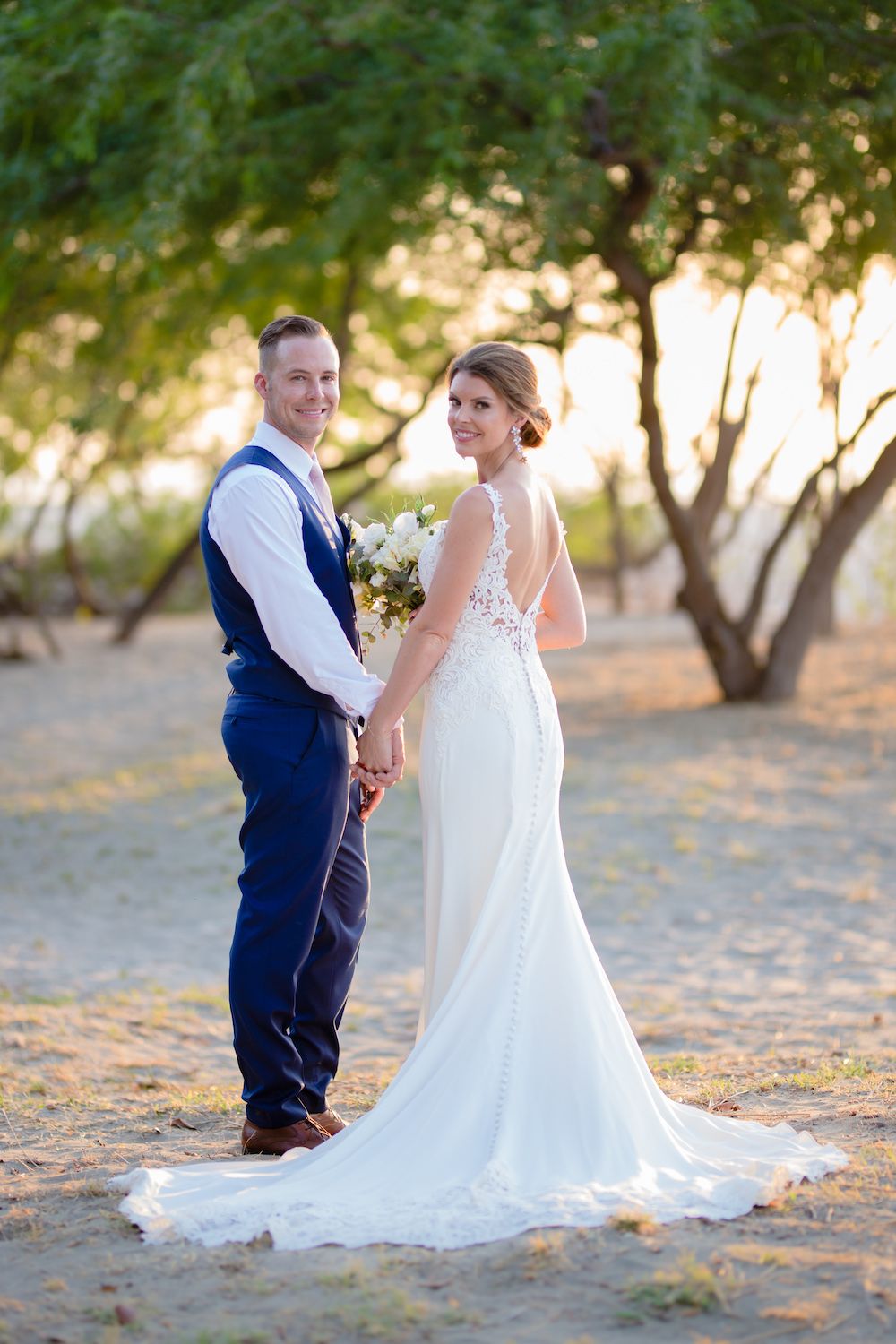 Bride and groom pose together at sunset under trees in outdoor wedding photo.
