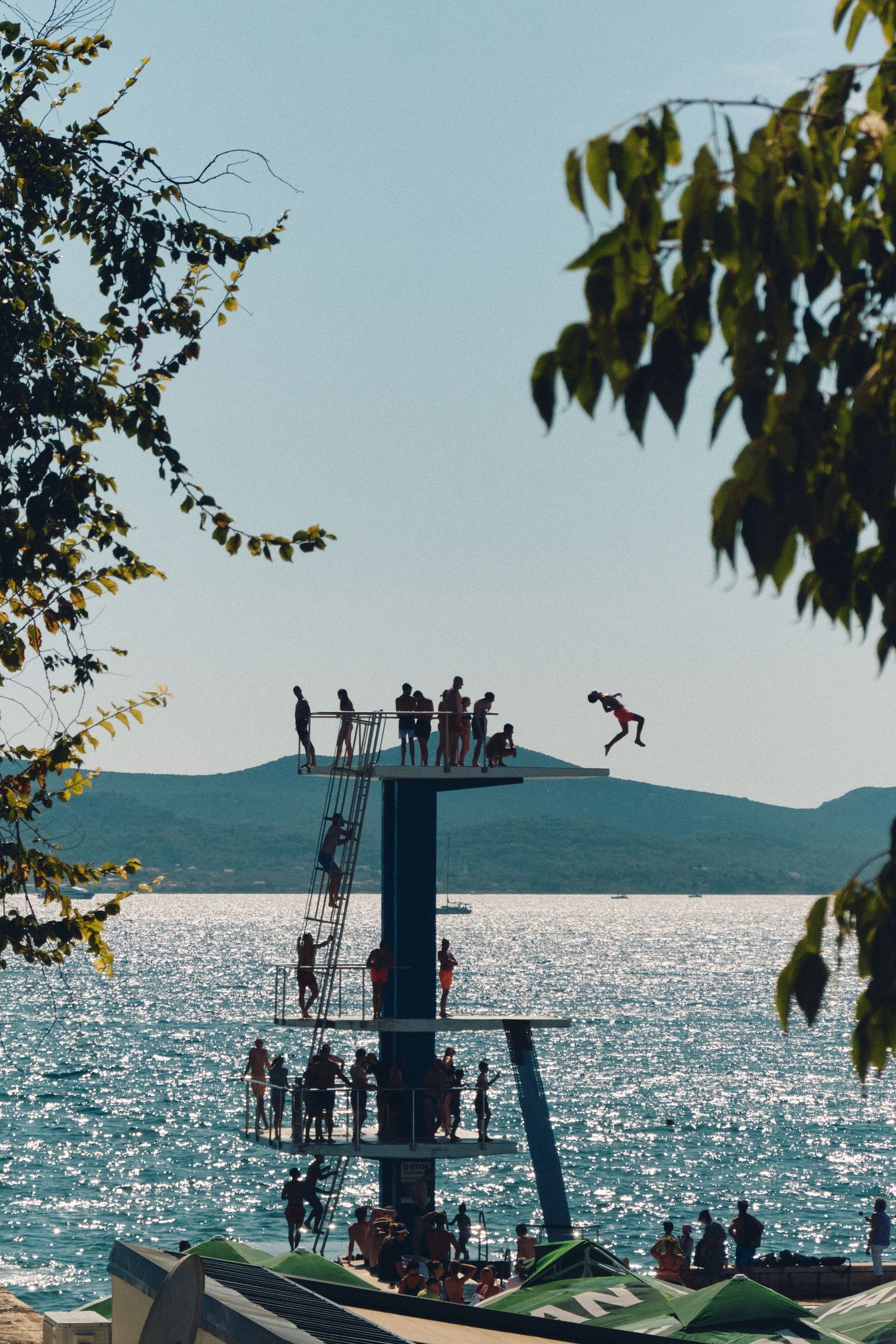 Silhouetted figures jumping from a multi-level diving platform against a sparkling ocean backdrop.