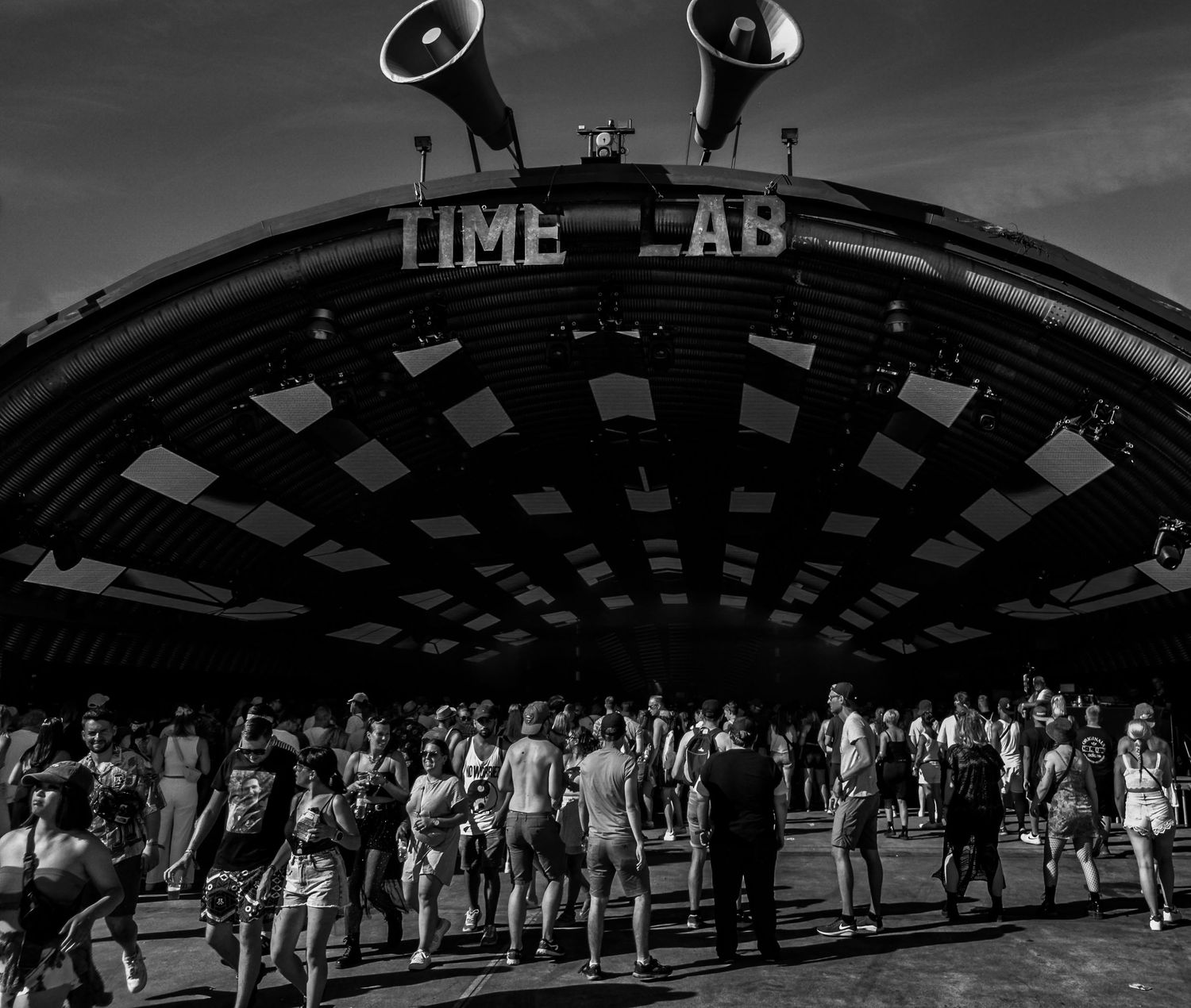A black-and-white photo of a large crowd gathered under an illuminated stage with "TIME-LAB" Parookaville Weeze Airport techno trance rave