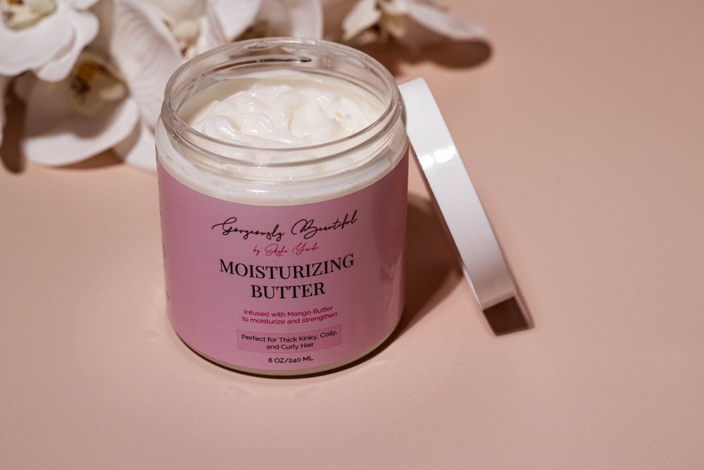 Open jar of pink moisturizing butter cream product with spatula.