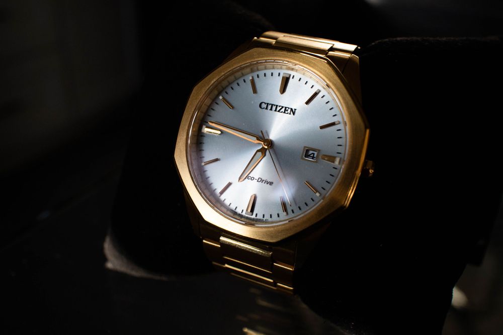 Close-up of gold Citizen watch with silver face against dark background.