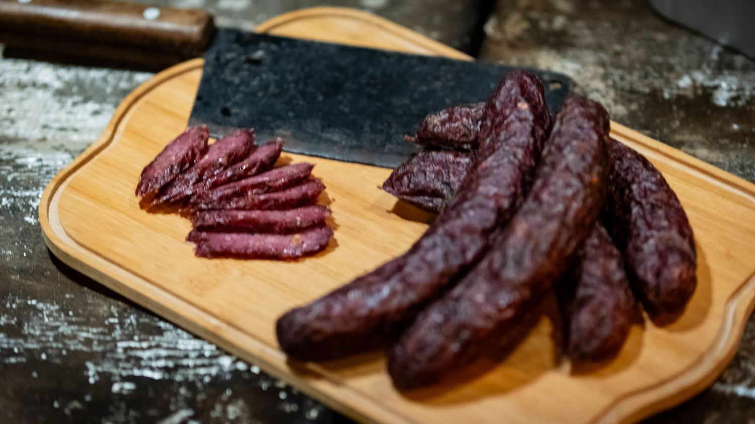 Dark red cured sausages and sliced meat displayed on a wooden cutting board.