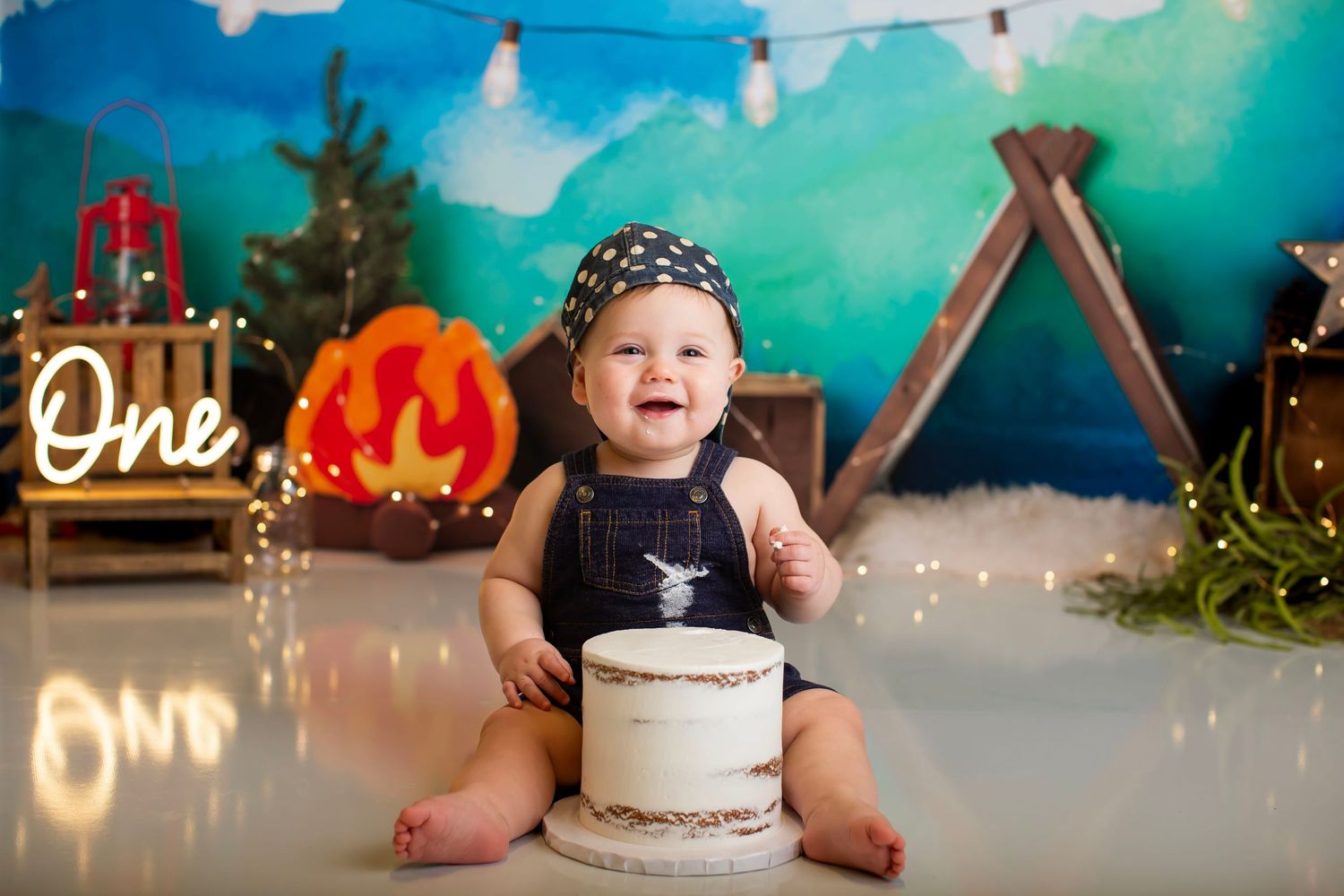 Baby seated with cake against blue backdrop with lit neon sign and pumpkin decorations.