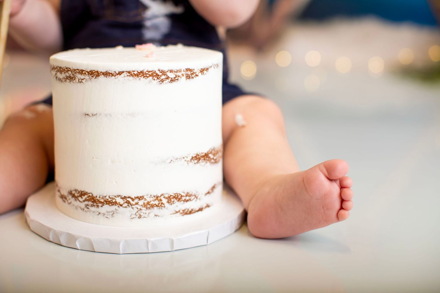 Close up of white frosted cake with tiny foot visible in soft focus.