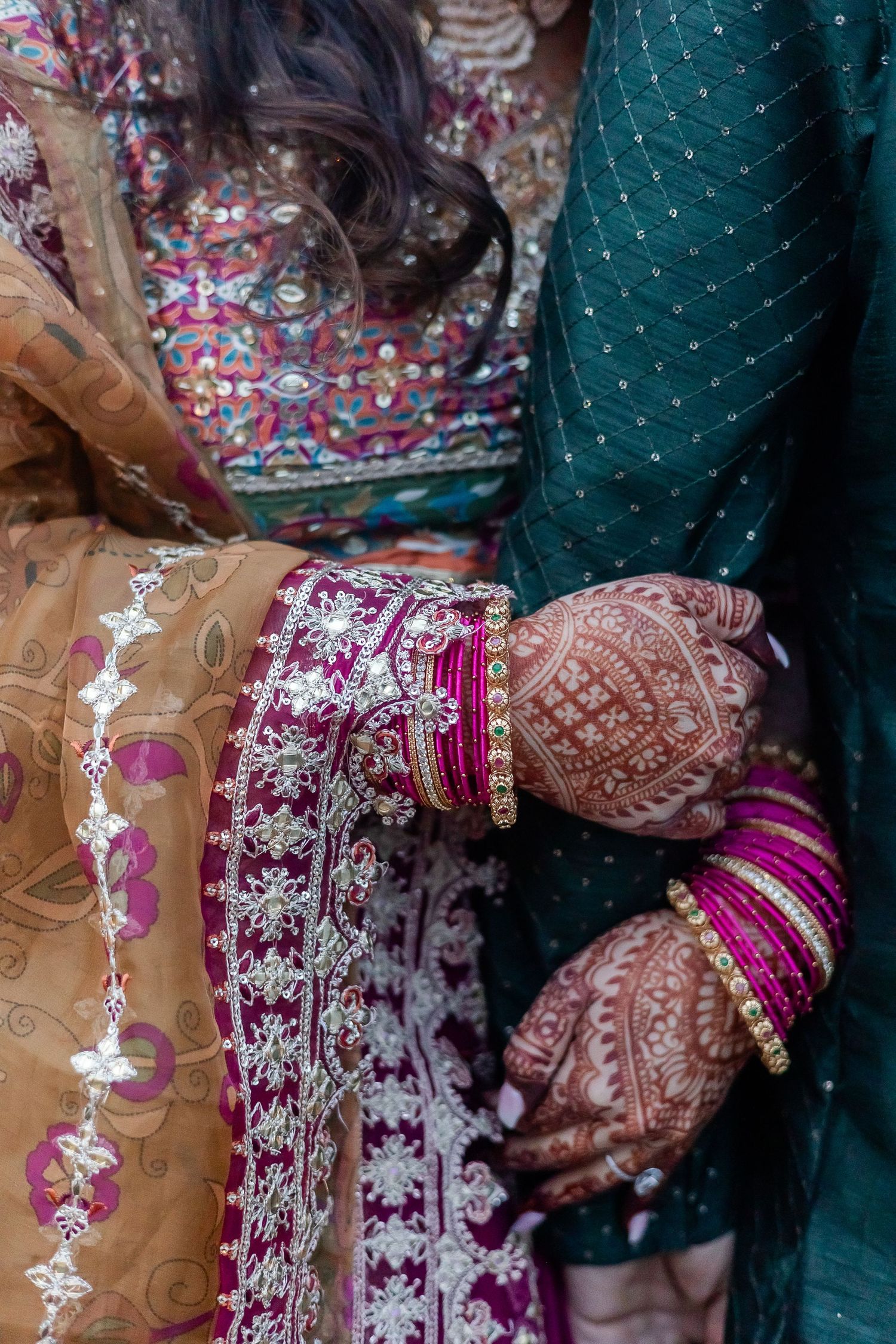 Detail shot of ornate South Asian wedding attire with bangles and henna designs.