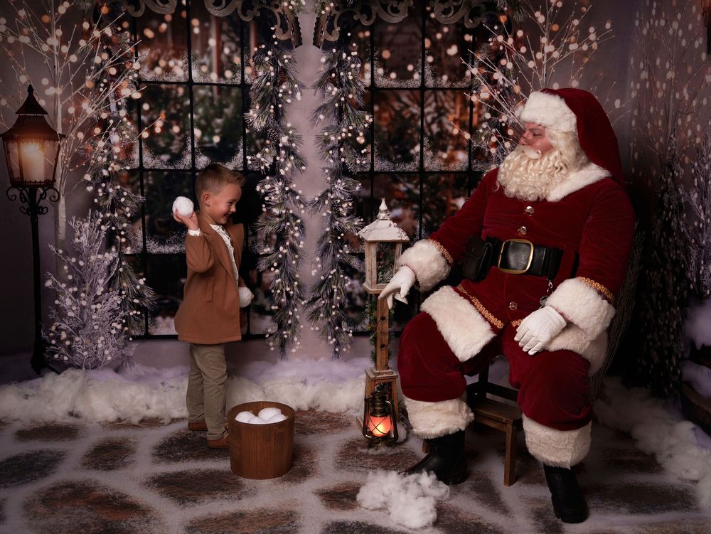 A festive winter scene shows a figure in a red suit sitting in a cozy chair surrounded by Christmas decorations and snow.