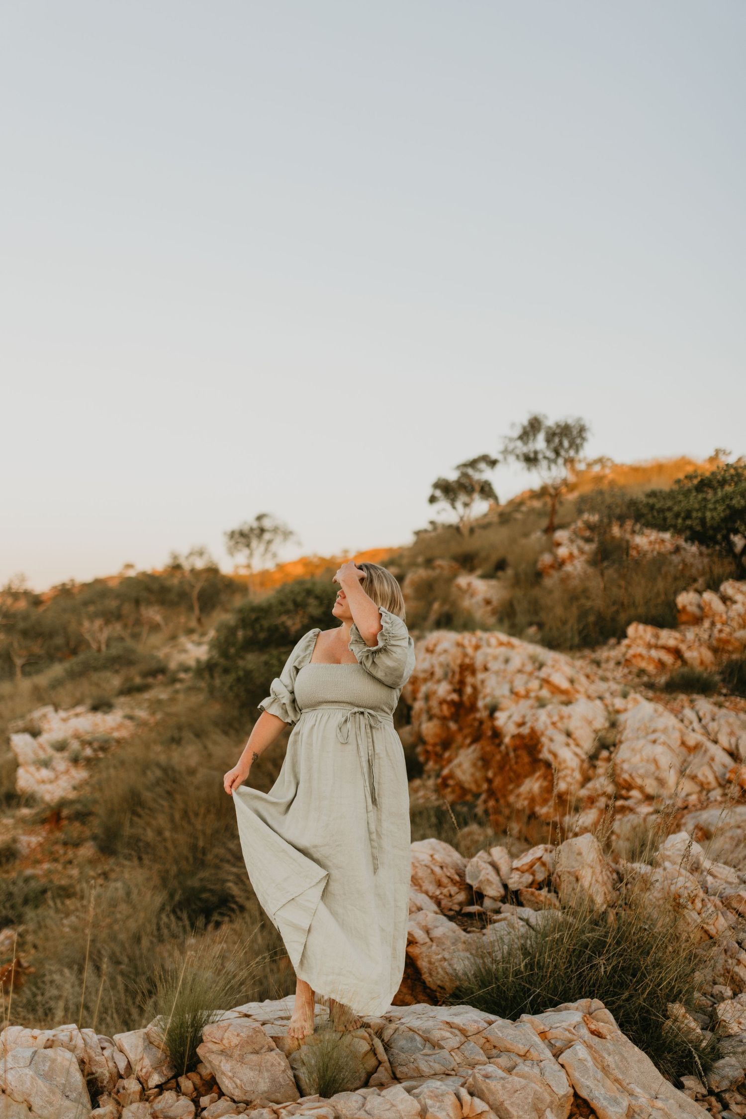 Woman stands on cliffs holding her dress at Lake Moondarra, Mount Isa