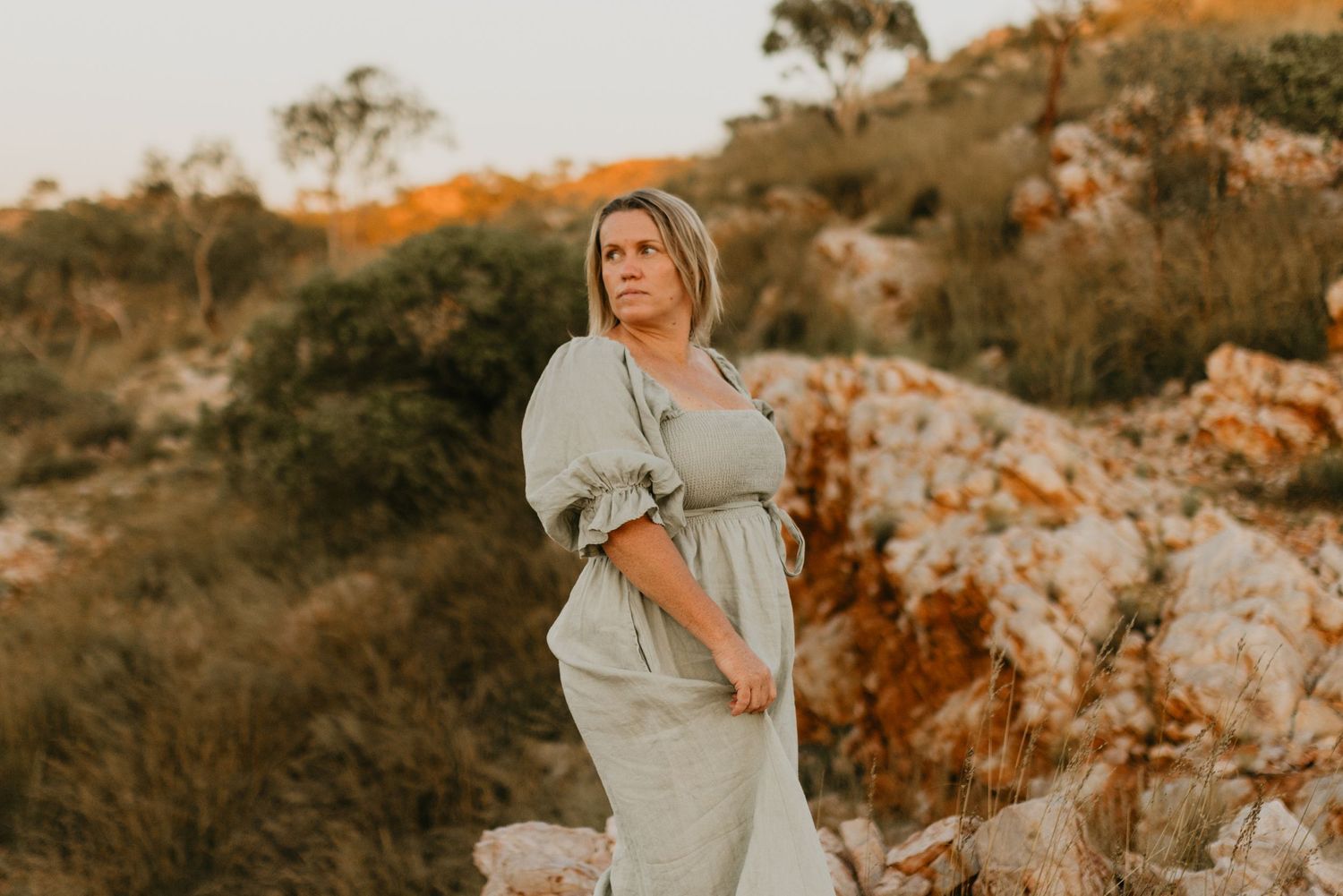 woman looks over her shoulder while standing on a rocky cliff at Lake Moondarra, Mount Isa