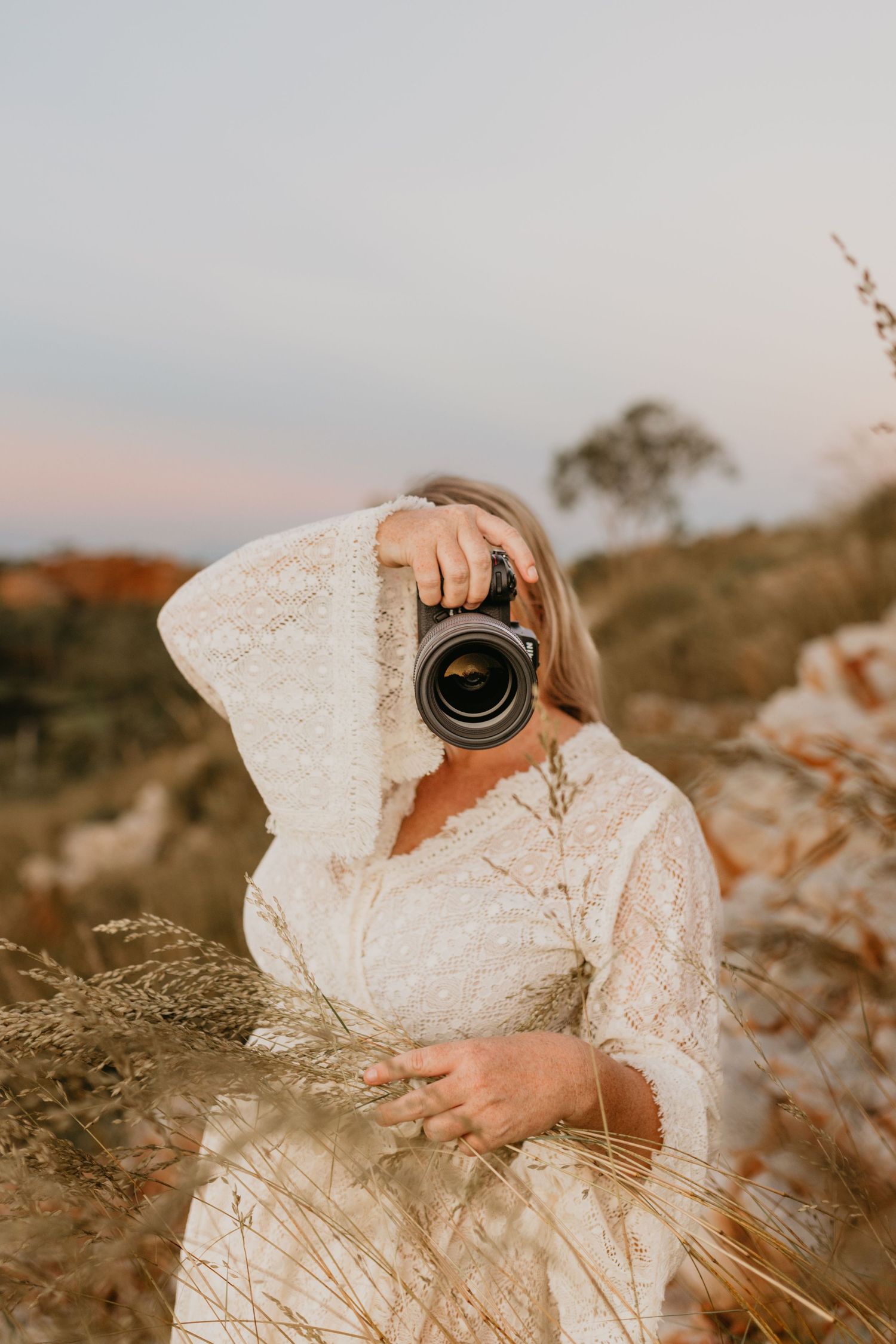 Woman taking a photo with foliage around her as the sun sets