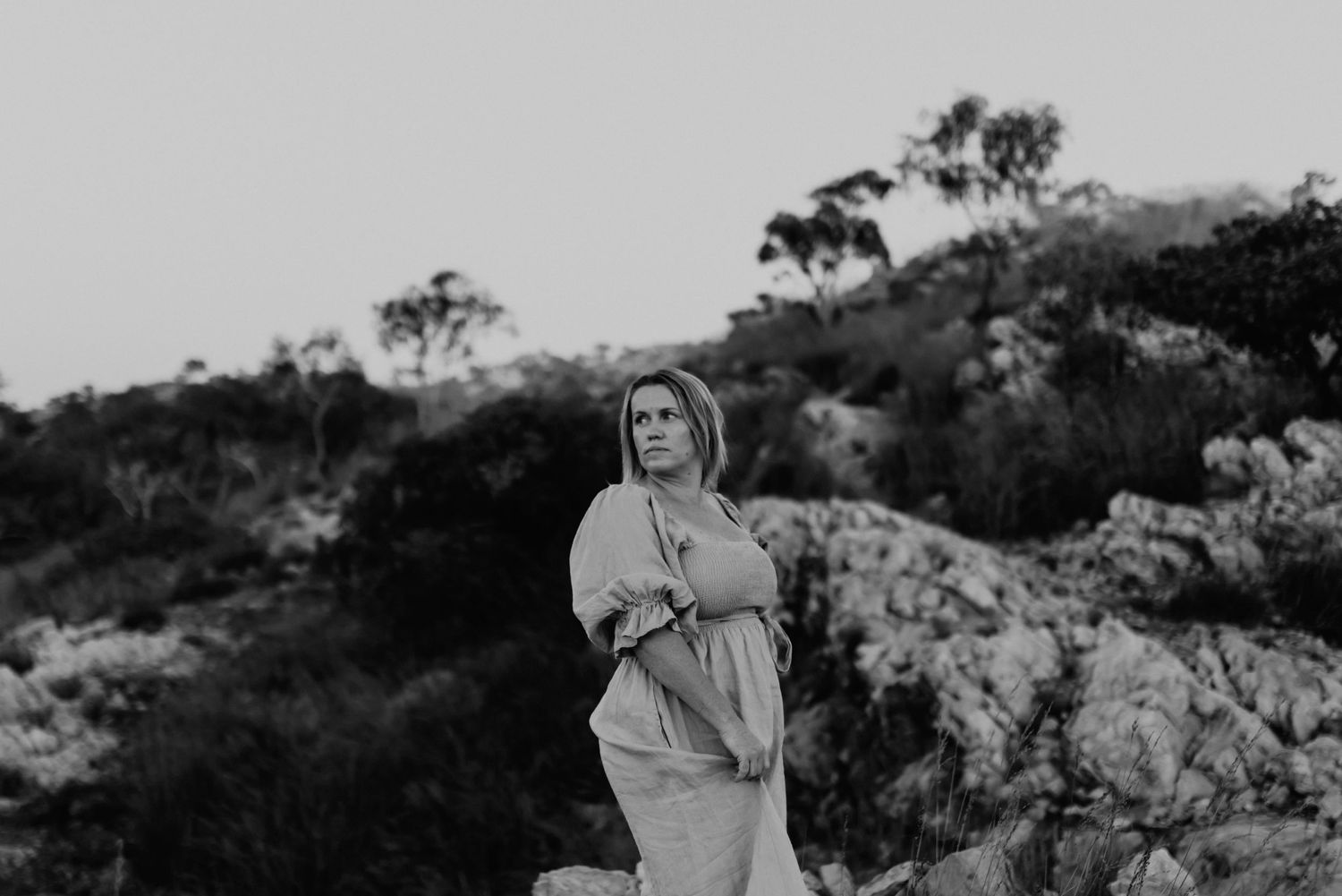 Black and white image of woman looking over shoulder while standing on cliffs at Lake Moondarra, Mount Isa