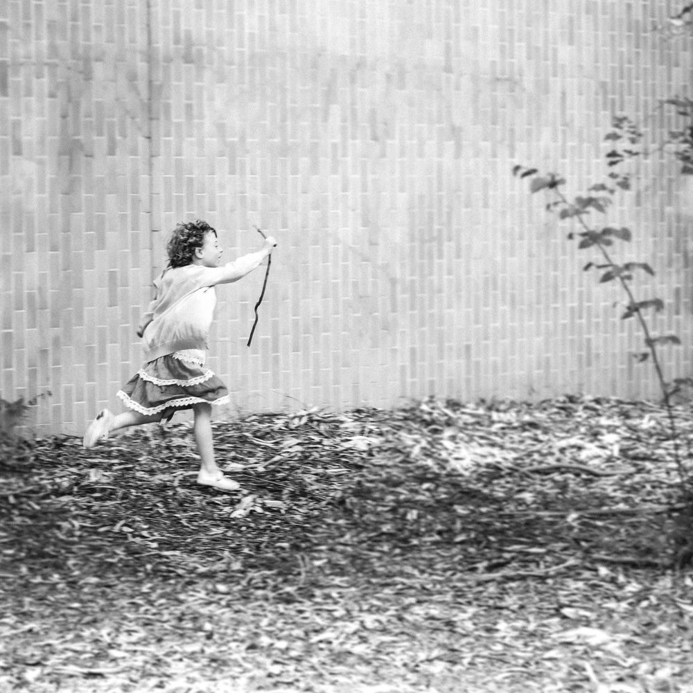 Vintage black and white photo of a small figure running with a stick outdoors.