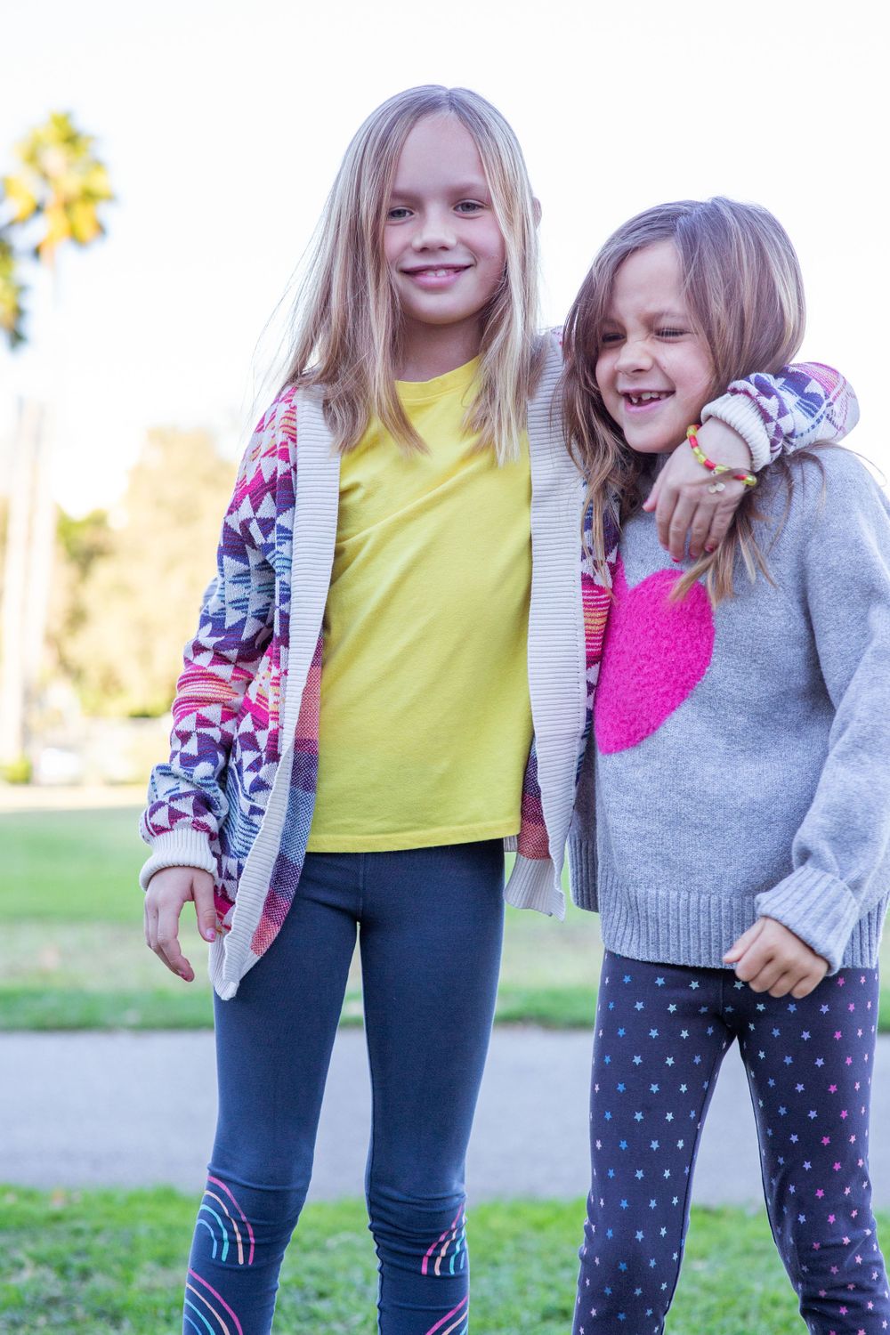 Two young friends in colorful sweaters sharing a joyful moment outside.