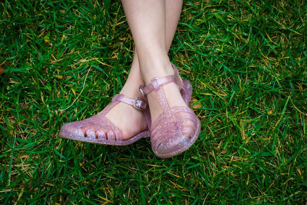 Pink jelly sandals on feet against green grass background.