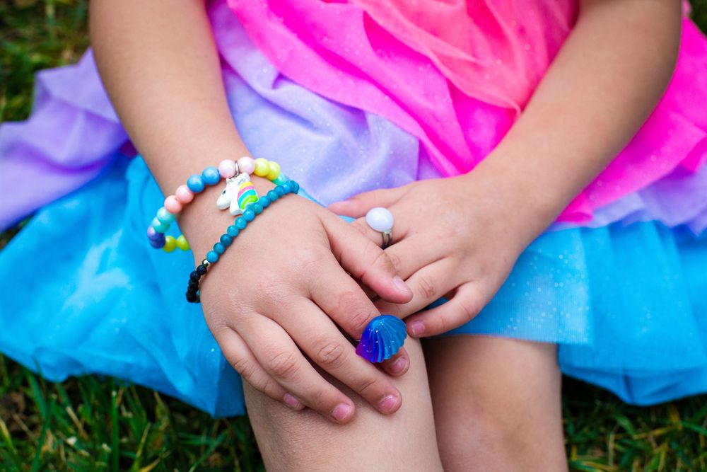 Colorful bracelets and rings adorning hands resting on a bright tulle skirt.