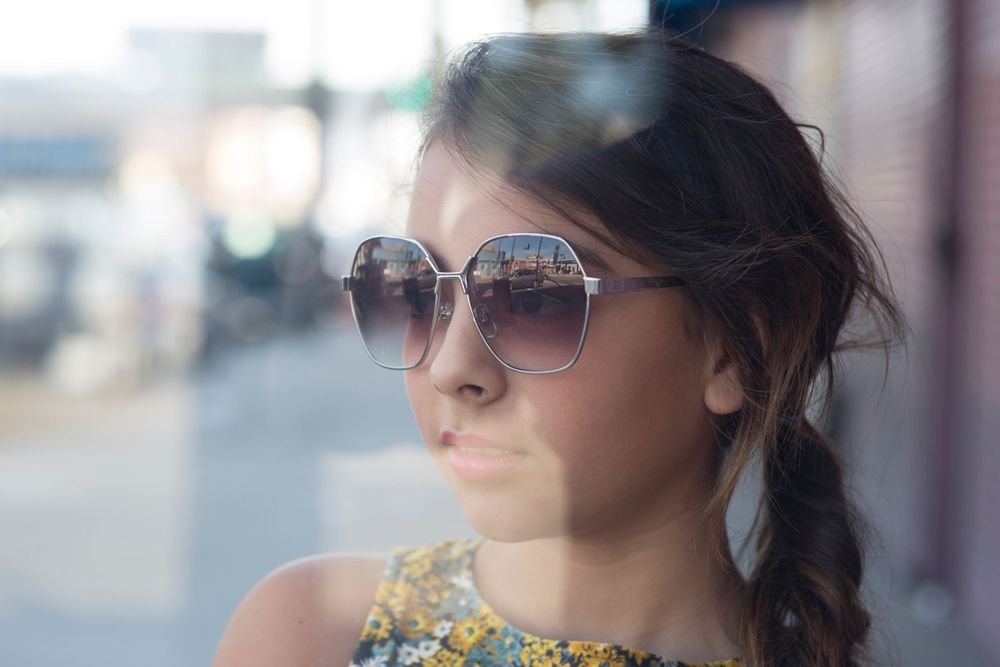 Artistic portrait with sunglasses and floral top in soft urban setting.