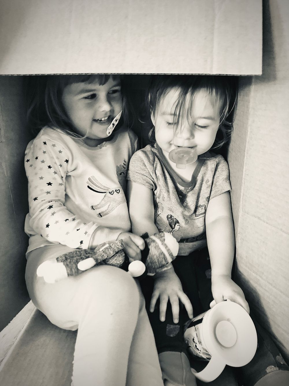 Two children laughing and playing together while sitting in a corner.