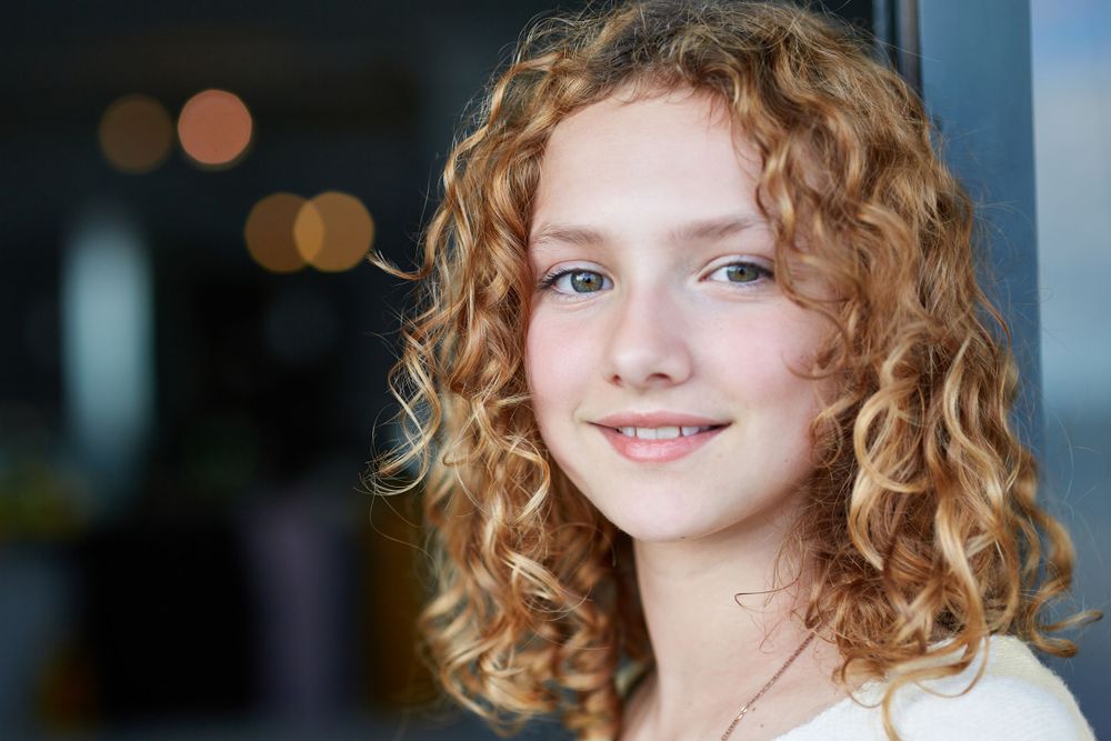 A candid portrait showing wavy golden curls and natural lighting against a soft blurred background.