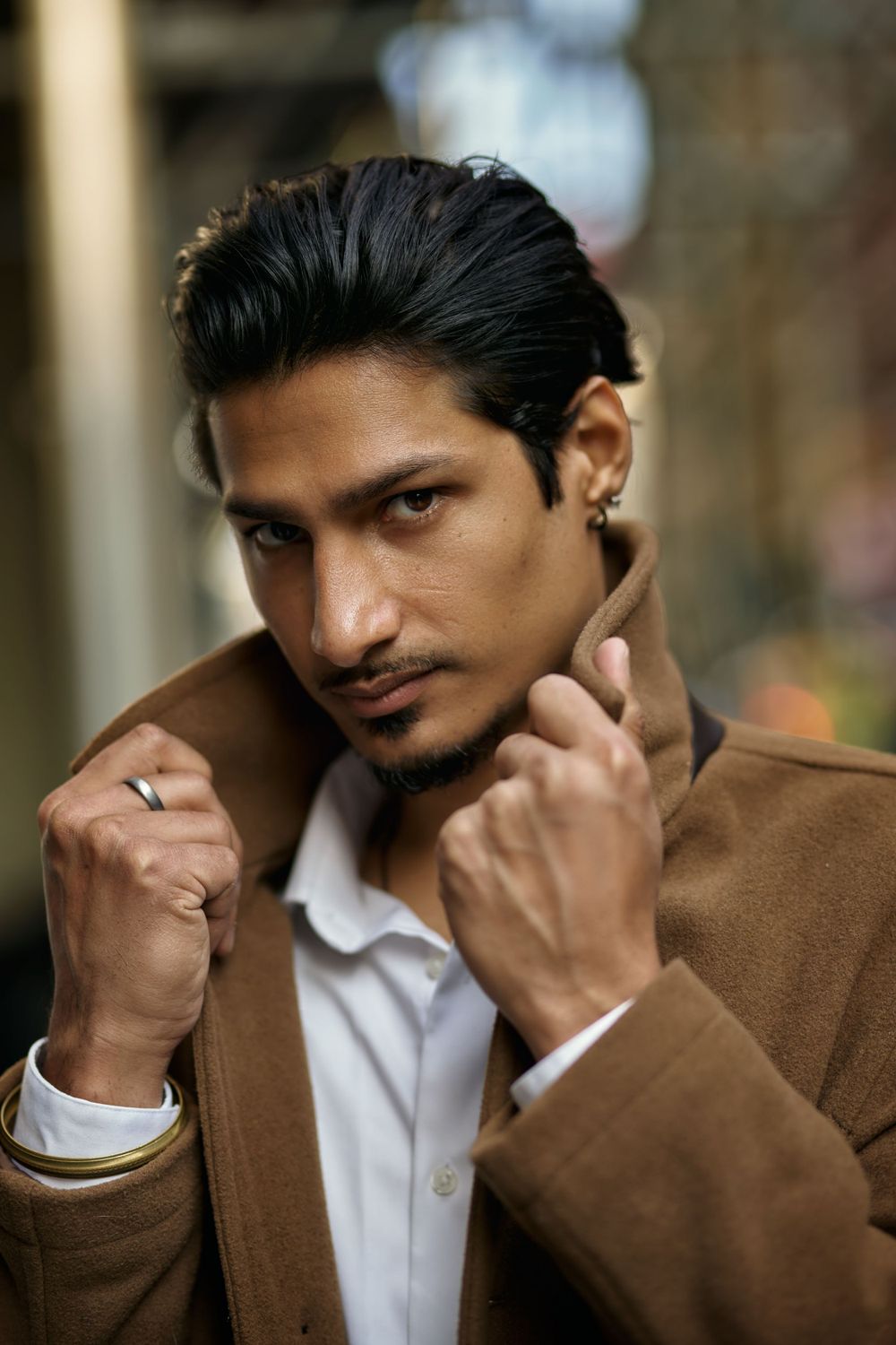 Professional fashion portrait showing brown suit jacket and white shirt against blurred background.