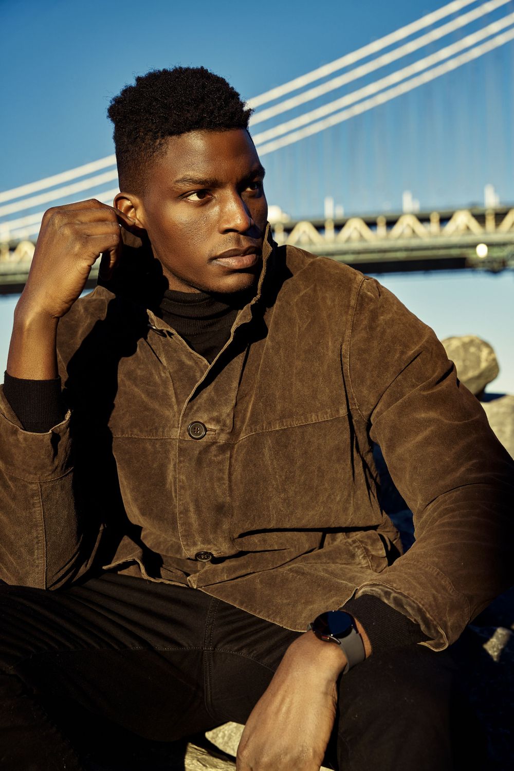 Outdoor fashion series showing brown corduroy jacket against bridge backdrop at sunset.