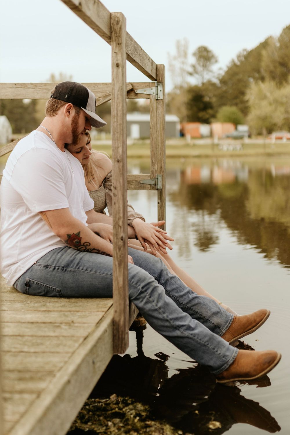 A couple sits together on a wooden dock overlooking a serene pond at sunset.