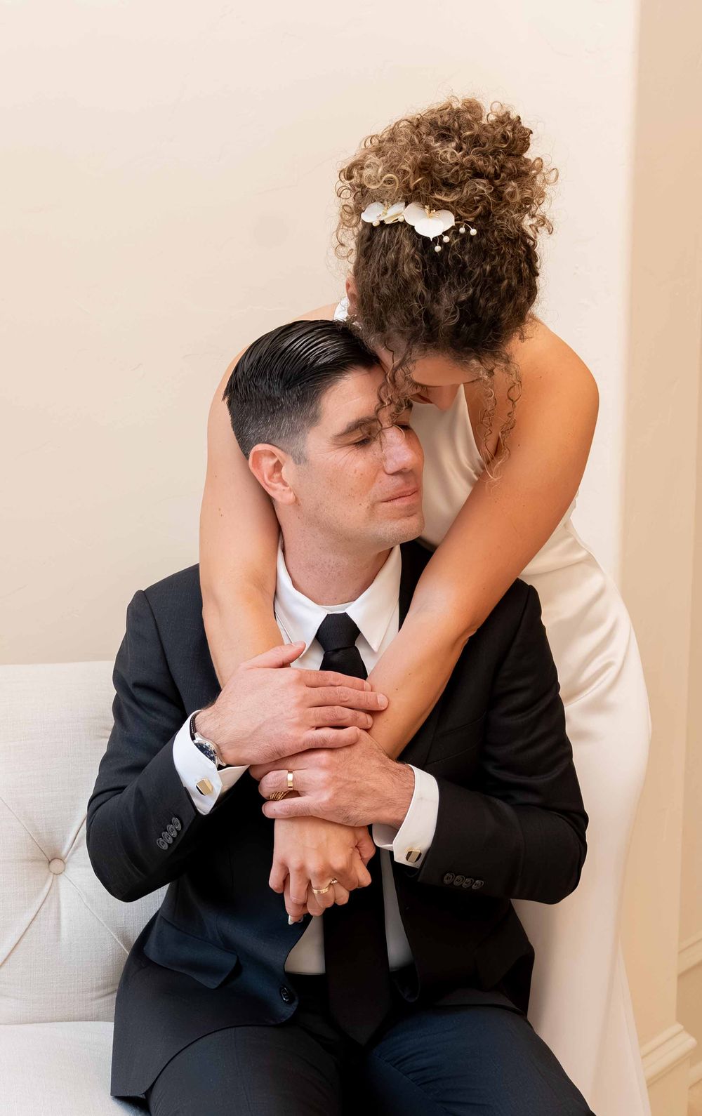 Bride embracing groom from behind in intimate wedding portrait, both in elegant white and black attire.