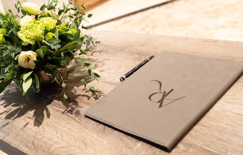 Elegant wedding guest book with monogram beside a yellow floral arrangement on a wooden table.