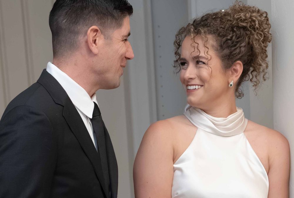A couple in formal attire sharing a tender moment, man in black suit and woman in white halter dress.