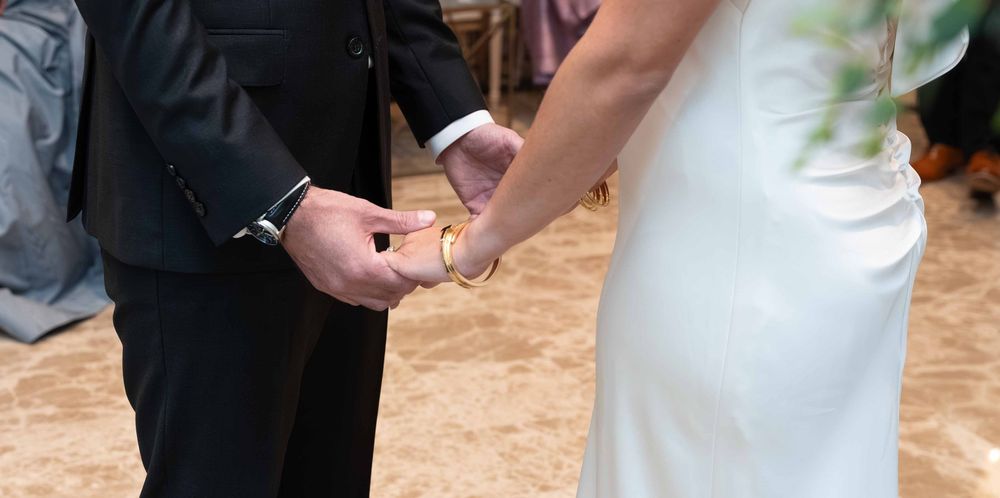 Bride and groom exchanging rings during wedding ceremony, bride in white gown, groom in black suit.
