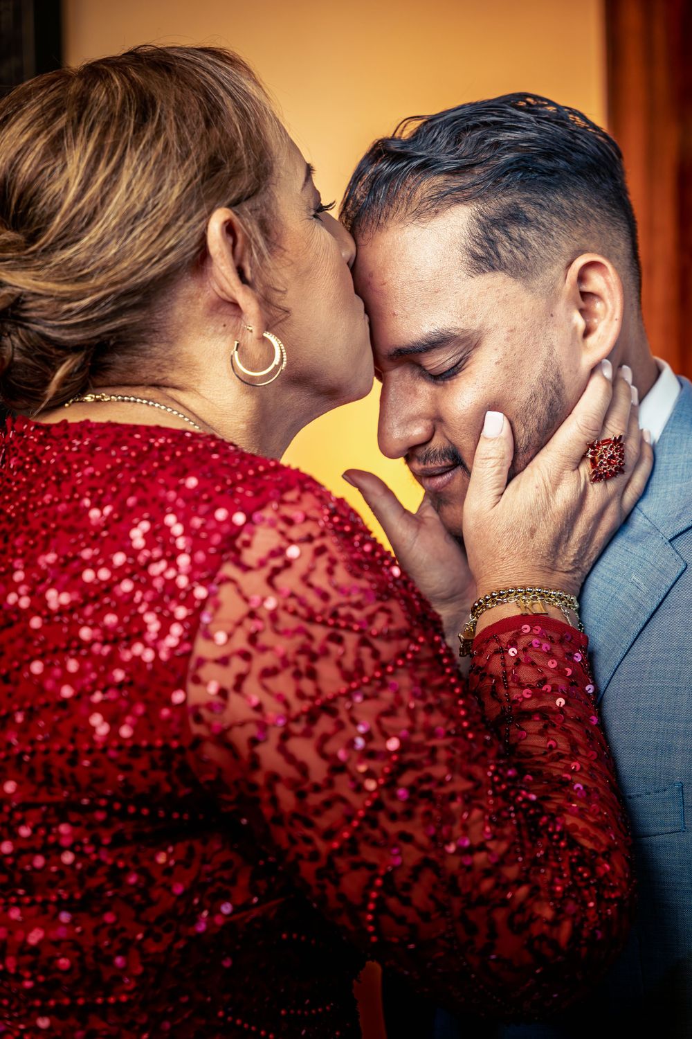 Romantic couple sharing an intimate moment with the bride wearing a sparkling red dress and groom in grey suit.