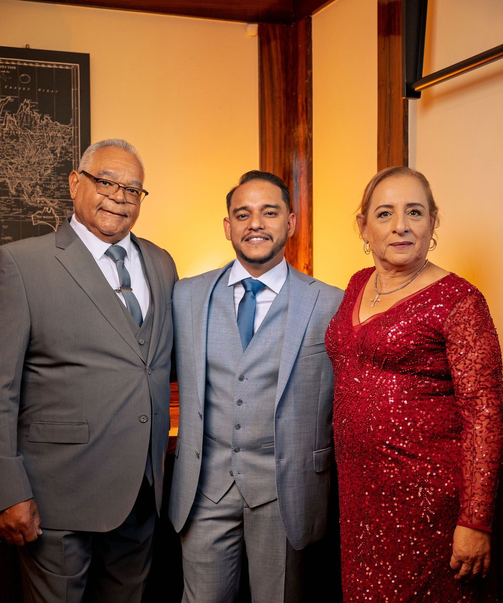Family members in formal attire pose together at a special event, with a woman wearing a sparkling red dress.