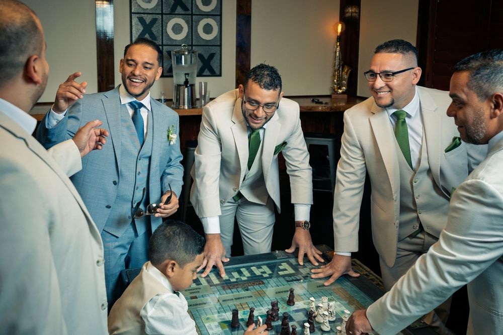 A group of men in suits and dress shirts gather around a table during a social event.
