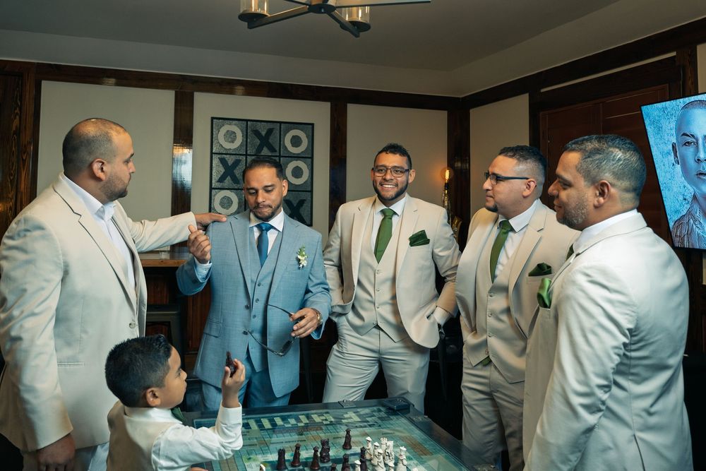 Groomsmen in light colored suits gather together in preparation for a wedding celebration.