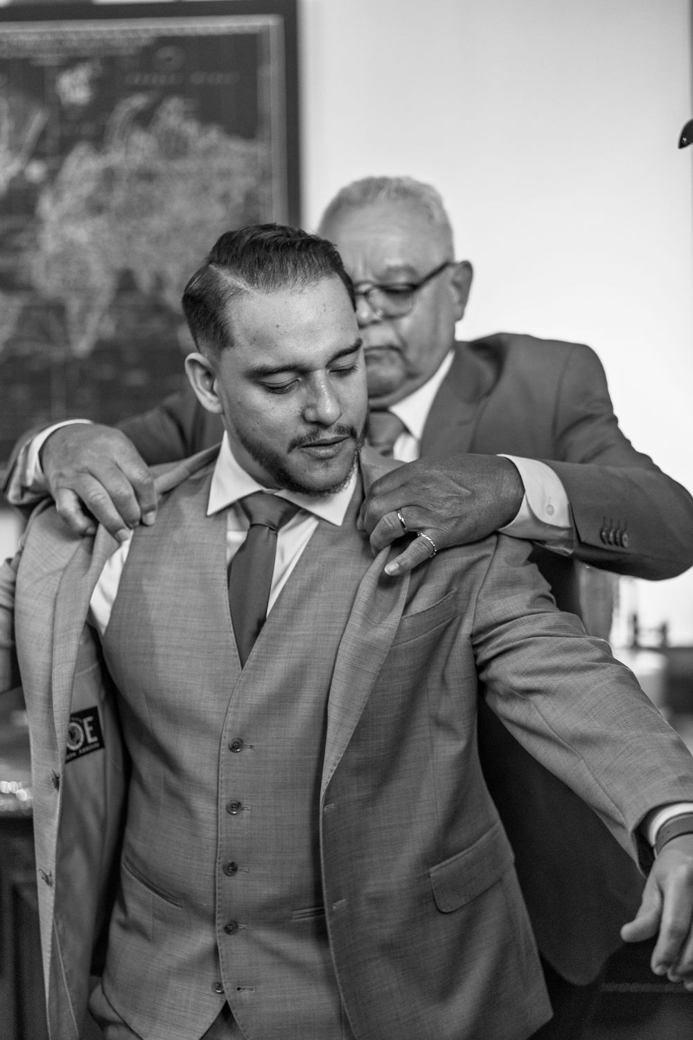 Black and white candid photo showing emotional moment between two men in suits at formal event.